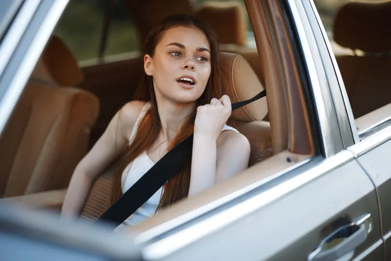 Young woman enjoying a road trip in a car, looking out the window with a relaxed expression, wearing a casual outfit, showcasing a sense of freedom and adventure.