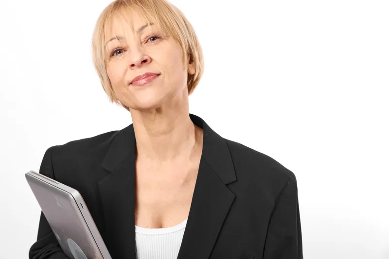 Woman business portrait, blonde hair, black blazer, holding a tablet, smiling in a white studio, communication and technology for professional online work, soft warm light