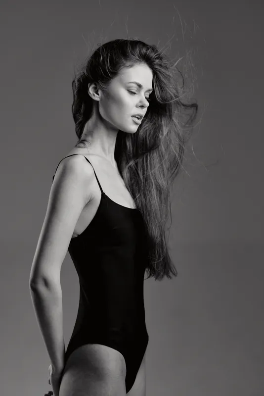 Black and white portrait of a slender woman with long hair in a black bodysuit expressing calm and elegance.
