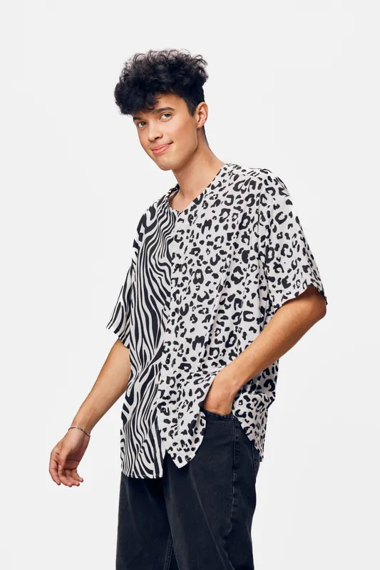 young man wearing patterned shirt and black pants stands relaxed against white background with casual smile expressing calm and confidence in modern style