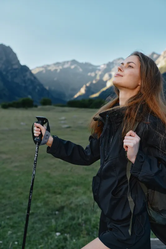 A focused outdoor adventurer is seen hiking with a trekking pole amid a scenic mountain landscape. She looks confident and calm, creating a peaceful and empowering outdoor atmosphere.