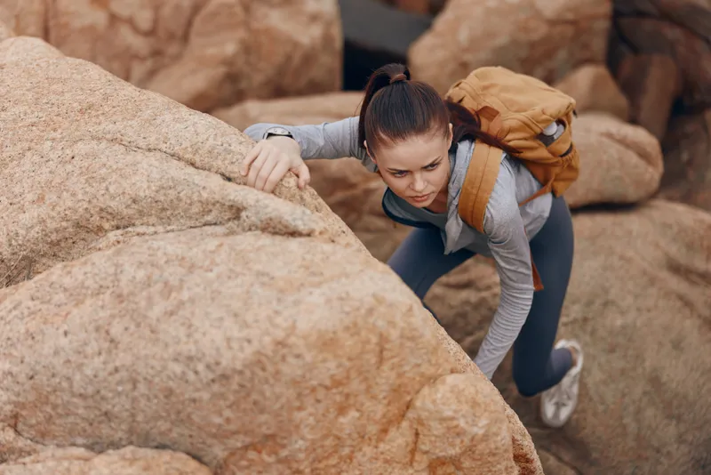 Young woman climbing rocky terrain, showcasing determination and strength, dressed in activewear, with a backpack, perfect for outdoor adventure themes