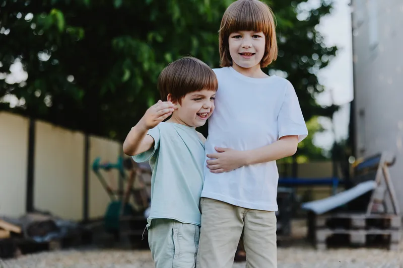 Two joyful boys standing together outdoors, smiling and enjoying their time. Their playful expressions capture the essence of friendship in a sunny atmosphere.