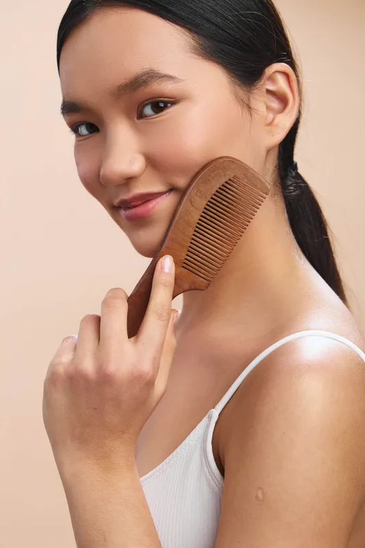 Asian woman gently combs her sleek hair in a softly lit studio, showcasing self care and calm confidence with a warm, inviting mood and a subtle healthy glow.
