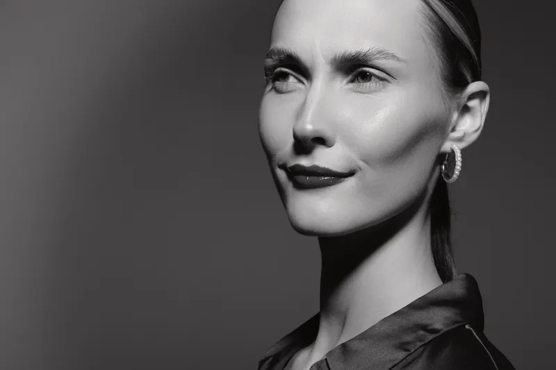 Portrait of a confident white woman with fair skin and slicked hair in black and white studio lighting.