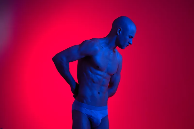 Athletic man posing under dramatic lighting, showcasing a strong physique with blue and red hues, creating a striking visual effect and dynamic atmosphere.