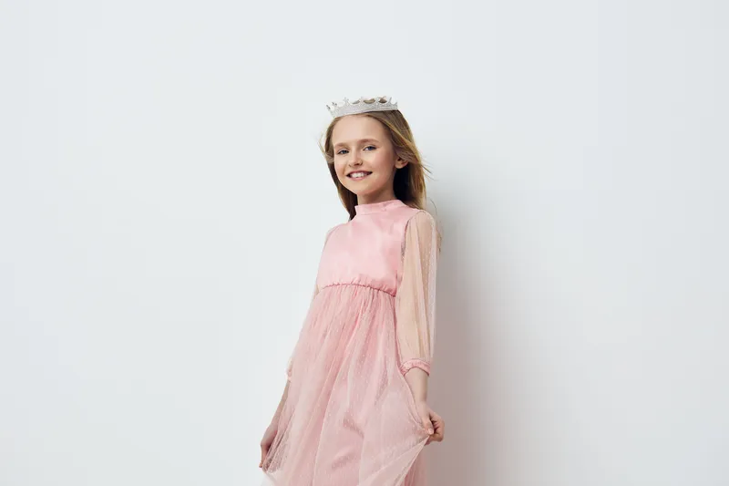 Smiling young girl in a pink dress, showcasing joy and innocence, against a simple white background, perfect for concepts of childhood and happiness