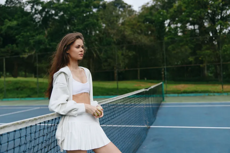 Young female tennis player in white sportswear reflecting on the court, showcasing determination and focus Bright green background enhances the vibrant energy