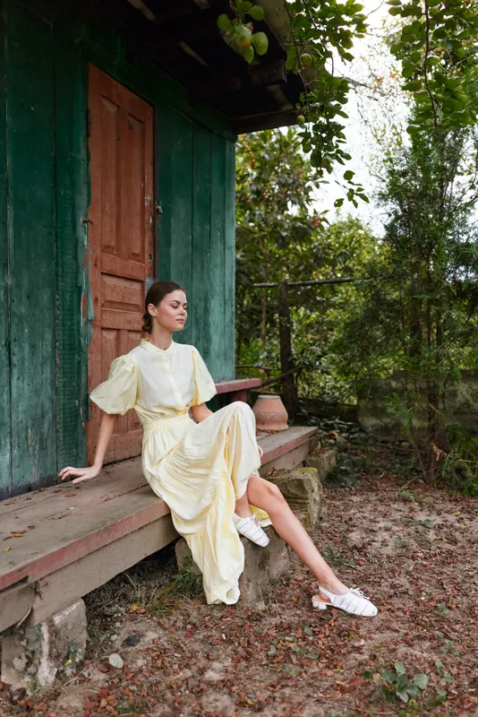 Woman sitting on cottage porch in dress, nature authenticity inclusivity