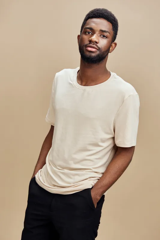 Young African man in a neutral toned t shirt posing confidently against a beige background, embodying a stylish and modern aesthetic