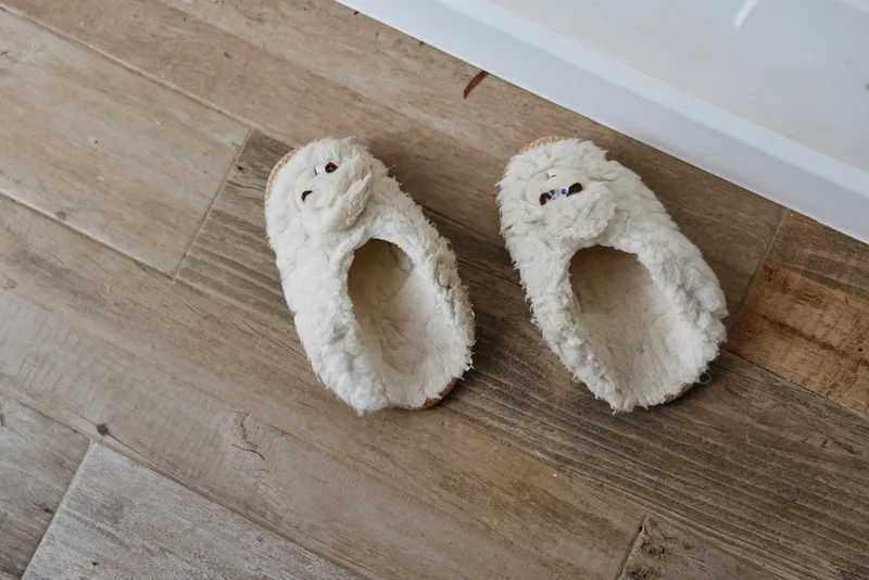 Cozy indoor scene features fluffy slippers resting on a warm wooden floor near a doorway, inviting a calm morning atmosphere and a relaxed home lifestyle moment for viewers