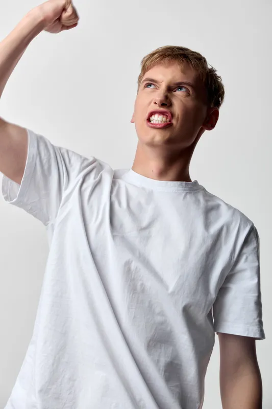 Anger, fist, protest, man, expression and emotion in a defiant gesture, a studio shot in a white shirt conveying tension, action, power, confrontation, and resolve for editorial use