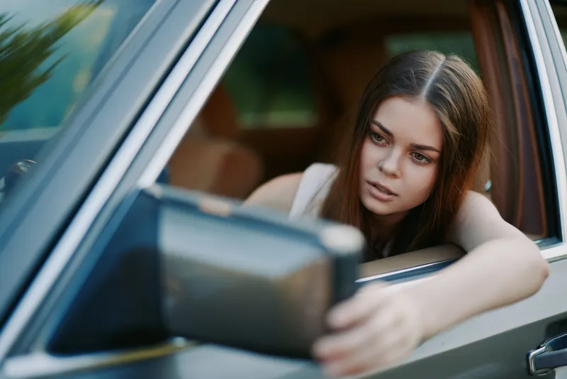 Thoughtful young woman looking out of a car window, embodying a sense of reflection and tranquility during a summer drive, set against a blurred natural backdrop.