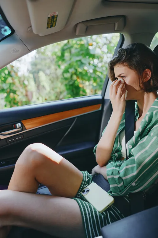 A woman sits in the car seat, resting her hand on her face, looking thoughtful and tired inside a calm car interior, conveying emotion and a pause during travel.