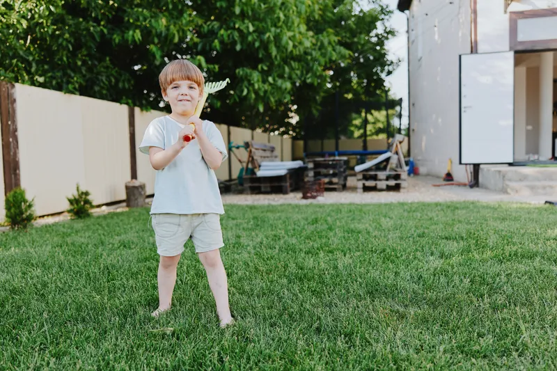 Happy boy playing outdoors with a toy airplane in a sunny garden, enjoying a playful moment in nature, surrounded by greenery and bright sunshine.