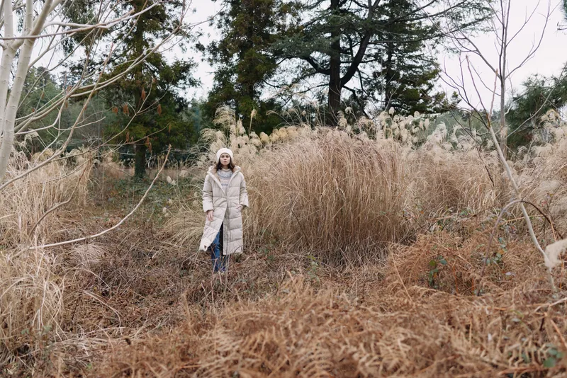 Winter scene with a lone person in a light coat standing among tall dried grasses in an open field, calm and natural, highlighting solitude and outdoor exploration.