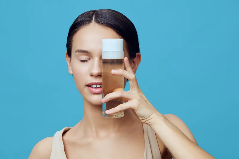 Young woman holding a skincare product in front of her face, promoting beauty and wellness Bright blue background enhances the fresh and vibrant mood