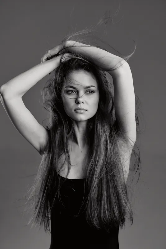 Black and white portrait of a young woman with long hair posing thoughtfully, showcasing natural beauty and elegance.