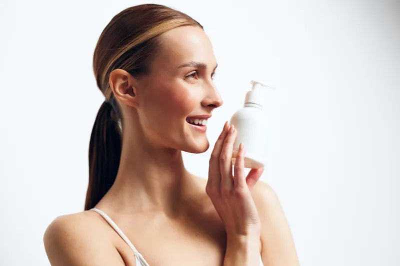 Woman holds candle near face in spa skincare beauty routine, gentle aroma and relaxation mood on white studio background, serene smile and profile portrait, calm glow