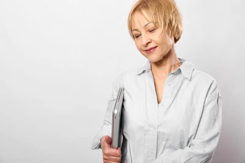 Elderly woman holding smartphone, looking down with tired expression, calm white studio background, concept of digital communication, aging, loneliness, technology use, portrait