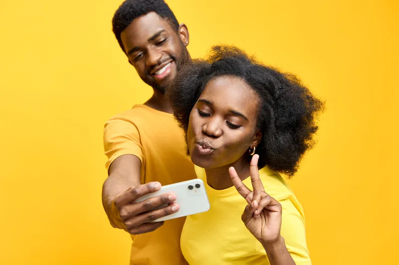 A cheerful young African couple taking selfies against a bright yellow background, showcasing joy and love while wearing matching colorful outfits