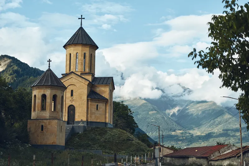 Church on hillside mountain landscape with historic stone architecture and chapel silhouette under cloudy sky