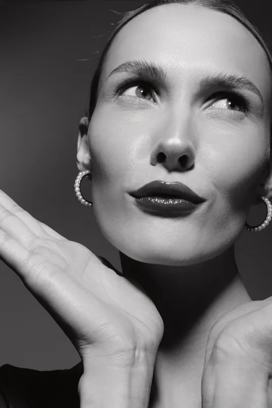 Close-up of a fair skinned young woman with slicked back hair and hoop earrings posing with hands near face. Concept for beauty, fashion, and elegance.