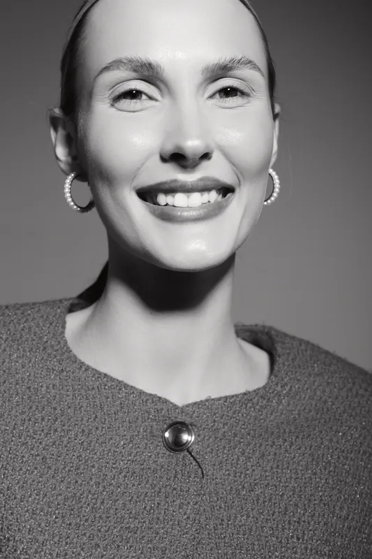 Smiling Caucasian woman with light skin and pulled back hair wears hoop earrings and textured top. Close-up portrait with soft lighting emphasizes natural beauty and positive emotion.