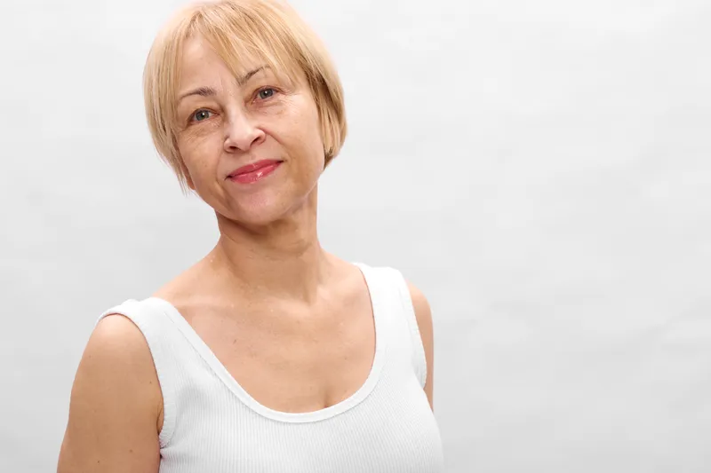 Smiling senior woman with short blonde hair, headshot portrait in studio light, soft neutral background, calm mature mood, friendly indoor beauty