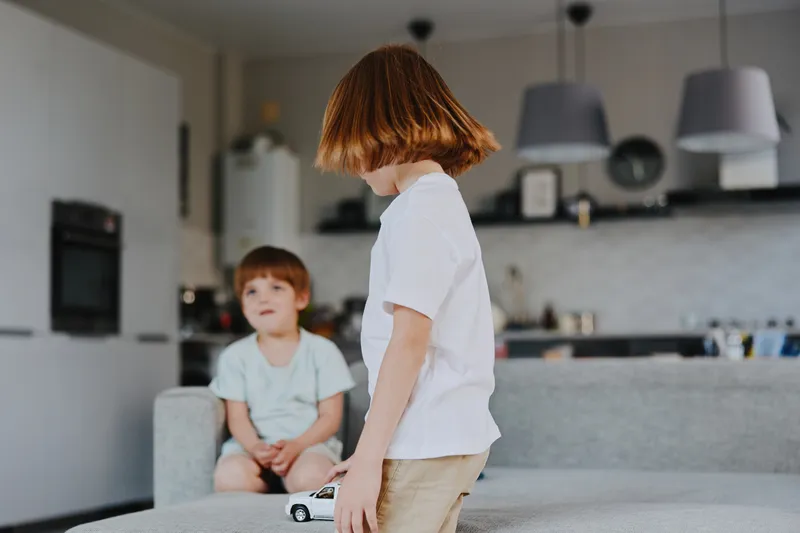 Curious boy playing with a toy car and a friend. Bright living room atmosphere with modern decor, showcasing playful childhood moments and creativity.