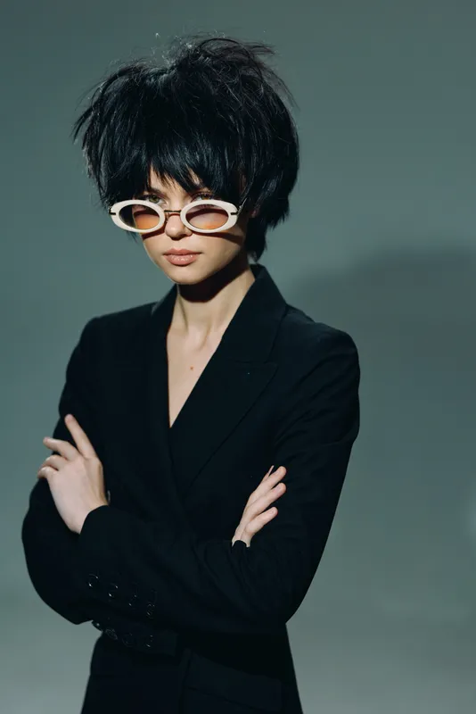 Stylish young woman wearing sunglasses and black blazer with confident pose in studio lighting