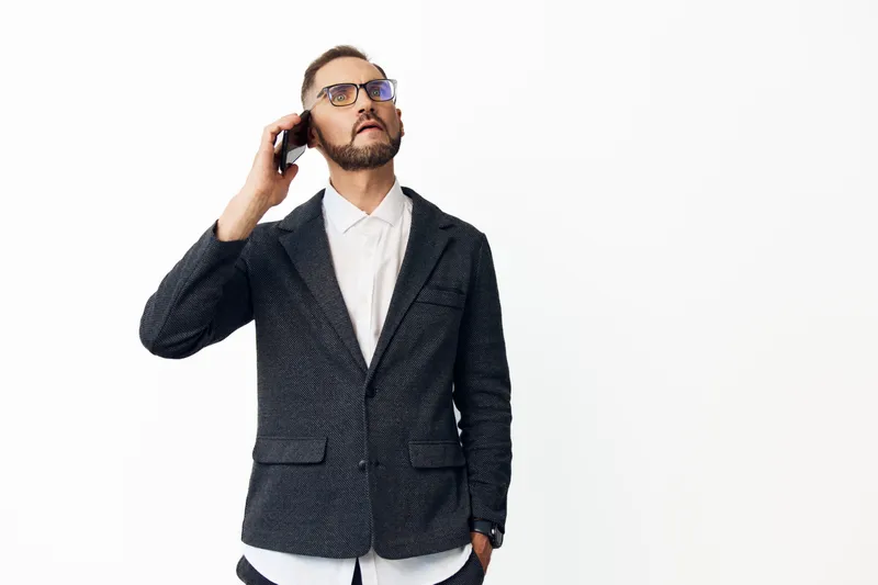 A professional business man on the phone stands against an isolated colored background, radiating confident focus and calm presence. He wears a dark textured blazer with a light shirt.