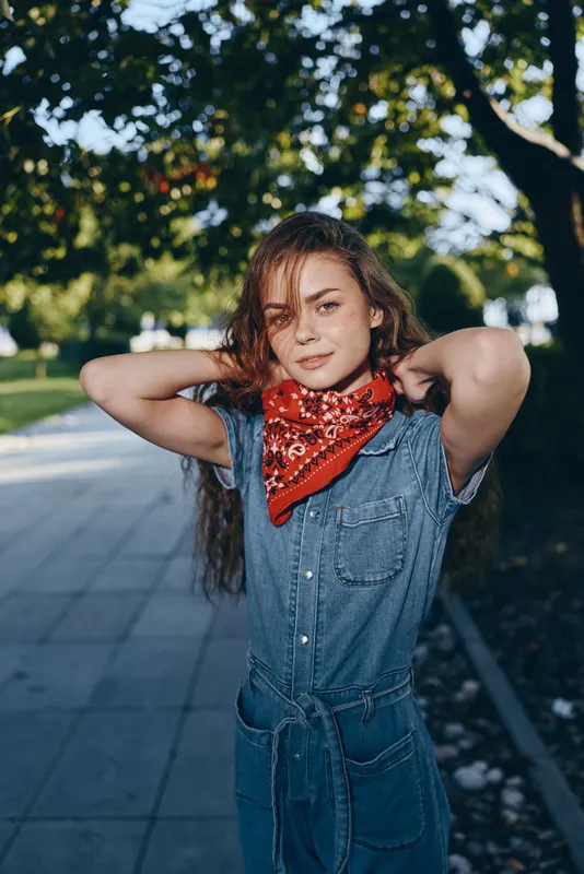 Lifestyle woman in modern boho-western denim street style wearing a red bandana, standing outdoors with natural light, casual and confident film color mood.