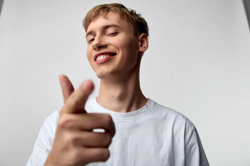 Smiling young man points at the camera in a casual white tee, creating a friendly lifestyle image suitable for social media, advertising, or cheerful brand storytelling and engaging visual