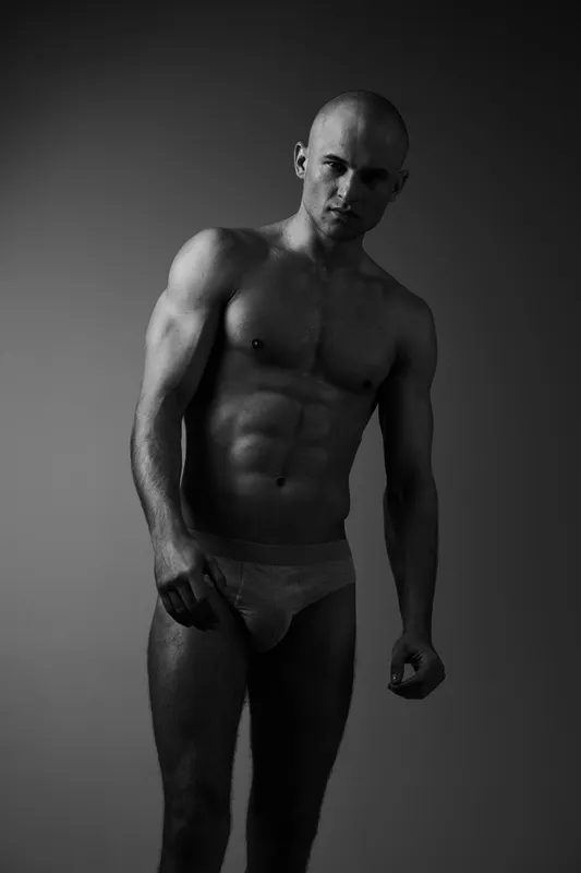 Black and white image of a muscular man standing confidently, showcasing his physique and strength, embodying determination and focus.