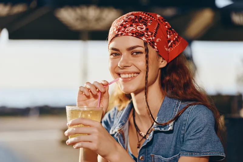 lifestyle woman in modern boho-western denim street style smiling with drink in hand, natural light, warm film color tone, casual outdoor setting, youthful vibe
