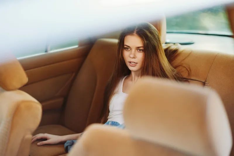 Thoughtful young woman in casual clothing sitting in the backseat of a car, reflecting on life with a serene expression, creating a warm and relaxed atmosphere.