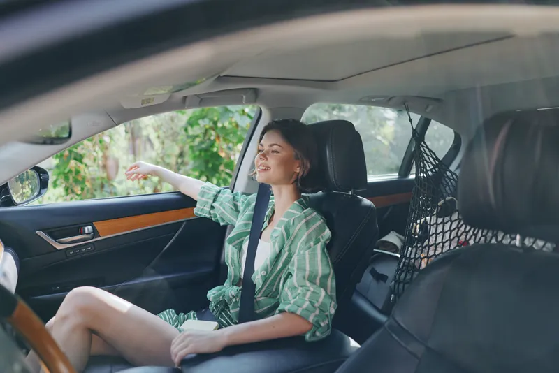 A young woman sits in the car seat with a calm smile, wearing a green striped shirt and a seatbelt, captured from the passenger side.