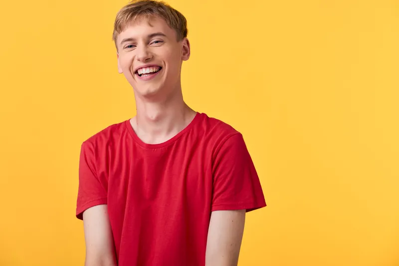 Smiling man in a red shirt stands against a bright yellow background, projecting cheerful energy and casual style suitable for lifestyle, fashion and happiness campaigns