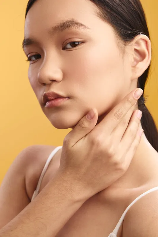 asian woman poses in a studio portrait with soft lighting, highlighting smooth skin and calm expression, creating an elegant, serene and confident vibe in a minimalist setting.