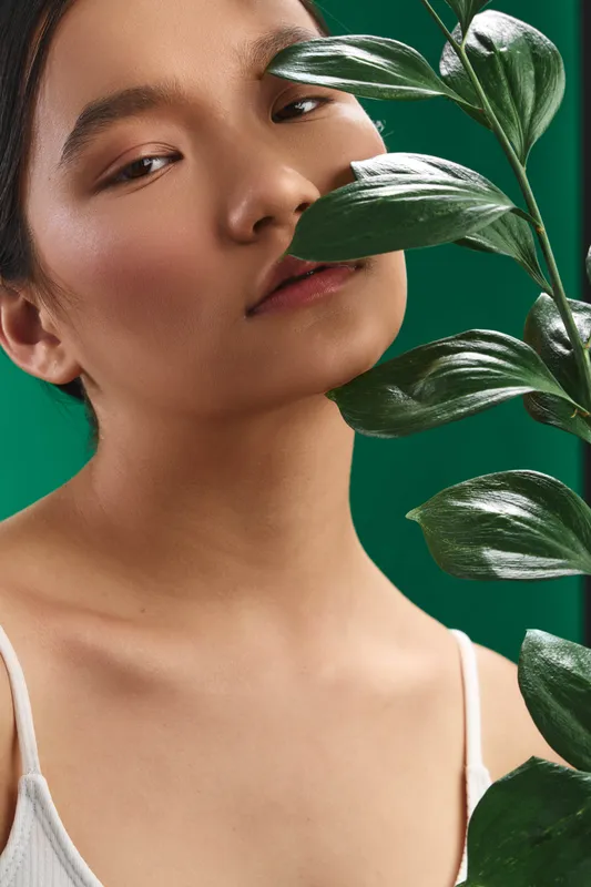 asian woman is photographed in a studio setting, gazing softly at a vibrant plant, the scene radiates calm energy with natural light, an intimate portrait highlighting beauty and tranquility.