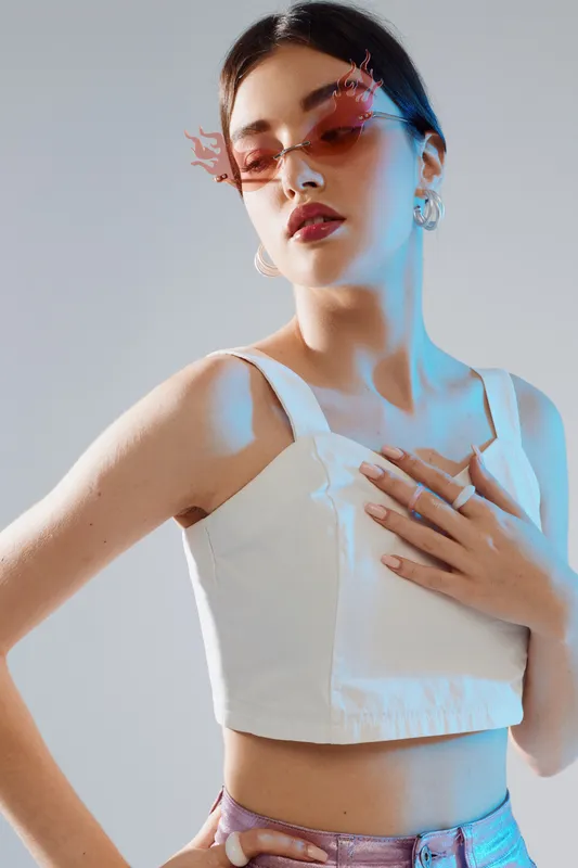 Young woman beauty fashion model poses confidently wearing stylish sunglasses and a white crop top. Studio shot with soft lighting on a neutral background. Concept of modern style.