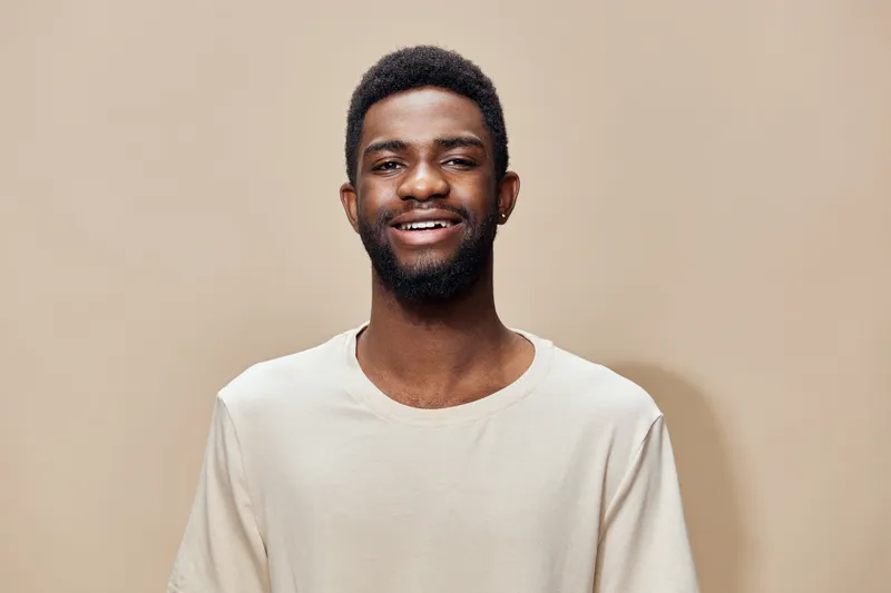 Smiling young man with a casual light colored t shirt against a beige background expressing happiness and confidence, perfect for lifestyle and wellness themes