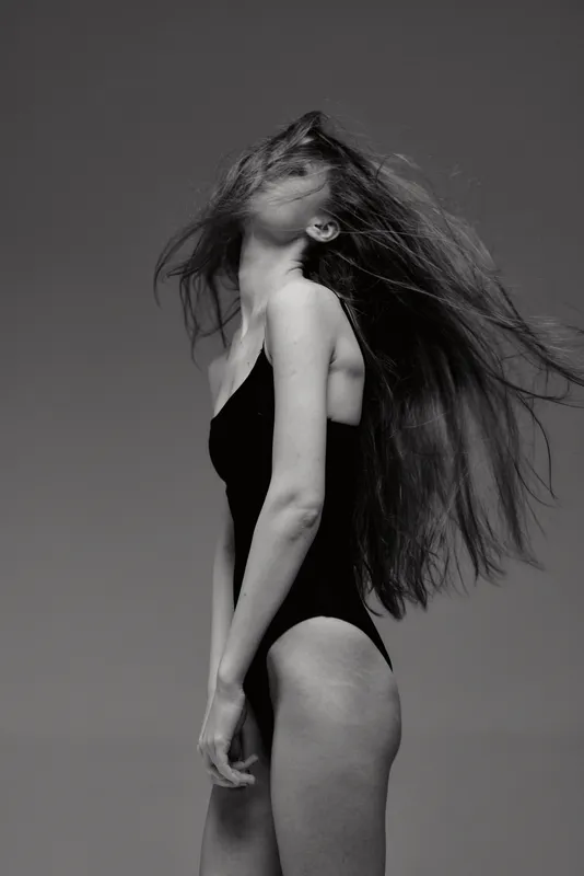 Black and white portrait of a woman with long hair in a swimsuit, expressing freedom and movement with a gray background