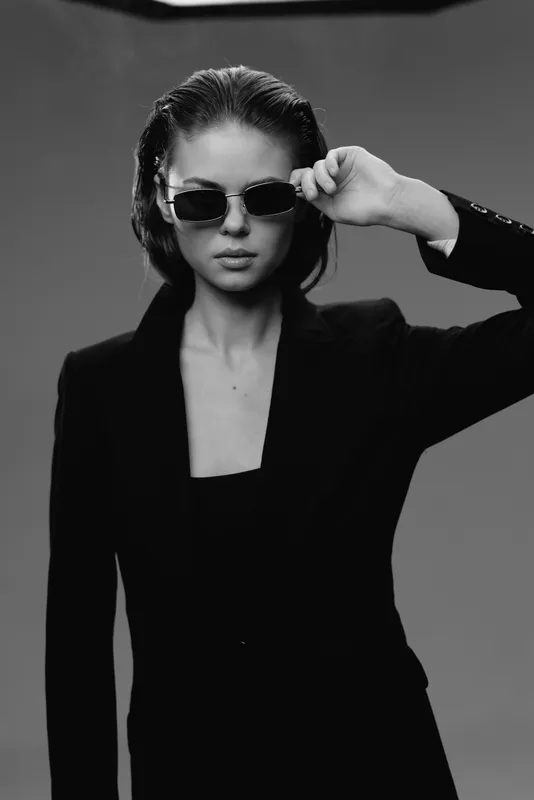 Black and white portrait of a stylish woman wearing sunglasses and a blazer with confident expression