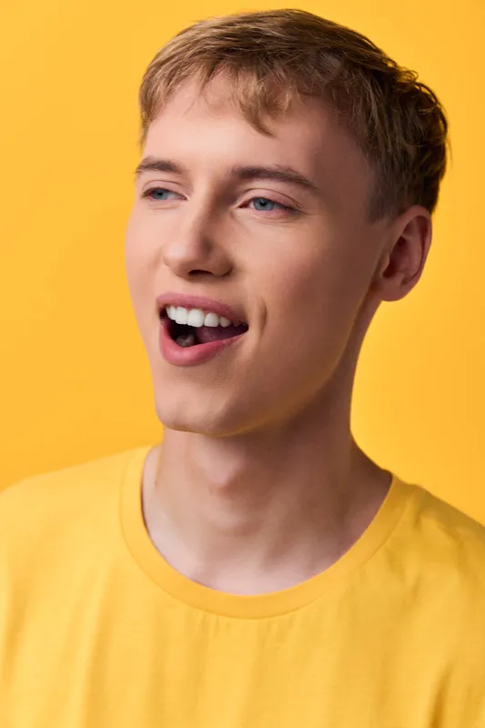 Cheerful young man with a bright smile wearing a yellow shirt against a vibrant yellow backdrop, conveying energy, enthusiasm, and positive mood for lifestyle and fashion concepts.