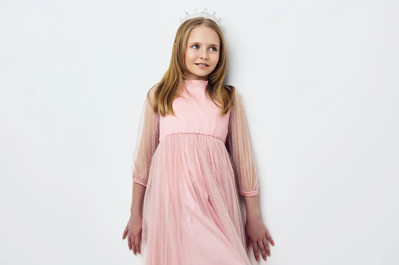 Young girl in a pink dress with sheer sleeves standing against a minimalist white background, exuding innocence and charm, perfect for children s fashion
