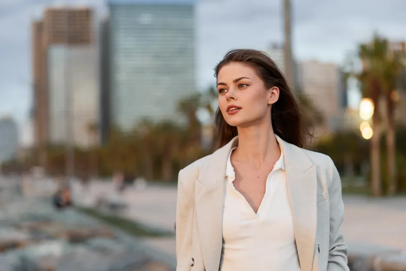 woman confident business professional walking outdoors in beige jacket with cityscape background and soft natural light urban lifestyle concept