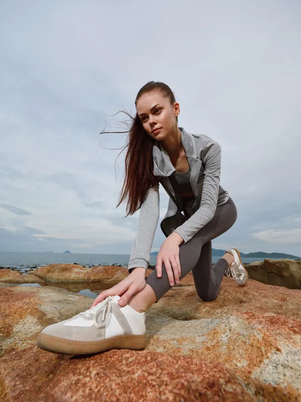 Young athletic woman stretching on rocky beach wearing sportswear, promoting healthy lifestyle and fitness concepts with ocean background
