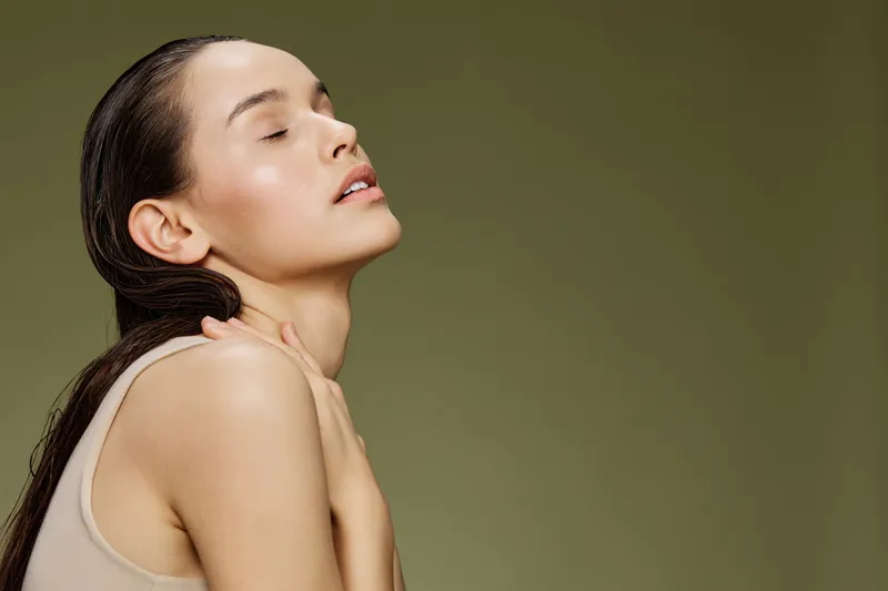 Beautiful young woman with long wet hair poses gracefully against a soft green background, exuding calmness and confidence in a minimalistic style